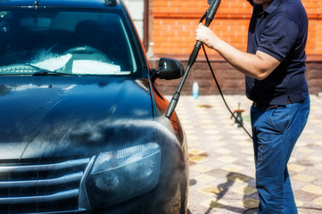Man washing his car under high pressure water outdoors.
