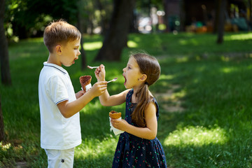 Little boy and girl eating waffle cones of ice cream in the park. Boy and girl feed each other ice cream.