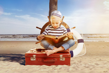 Child as a sailor reading a book on the beach - obrazy, fototapety, plakaty