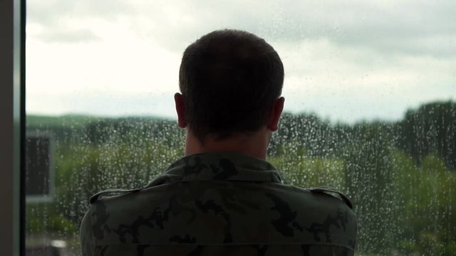 former military man stands by the window, it is raining