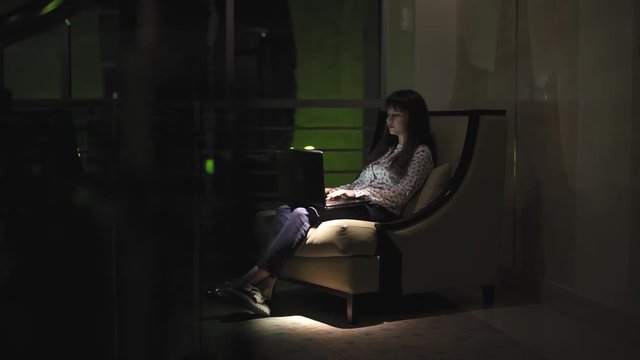 girl sitting by the window with a laptop in the evening