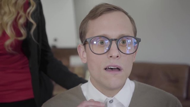 Blond sensual woman suddenly kissing the cheek of modestly dressed man in glasses. The nerd surprised, confused and shocked, he is shy. Beautiful lady flirting with the guy