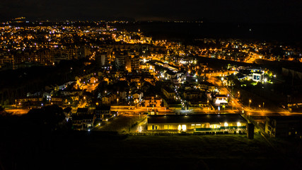 Aerial night view of the city and sea of ​​Anzio, near Rome, Italy. The lights of street lamps, car headlights and houses illuminate the urban landscape.