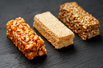 Cereal granola bar with peanuts, sesame and sunflower seeds on a cutting board on a dark stone table. View from above. Three Assorted Bars