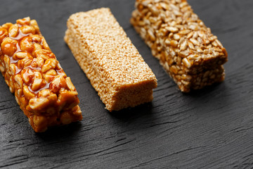 Cereal granola bar with peanuts, sesame and sunflower seeds on a cutting board on a dark stone table. View from above. Three Assorted Bars