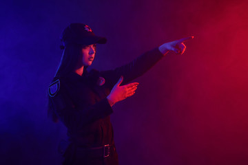 Redheaded female police officer is posing for the camera against a black background with red and blue backlighting.