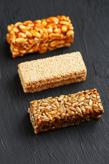 Cereal granola bar with peanuts, sesame and sunflower seeds on a cutting board on a dark stone table. View from above. Three Assorted Bars