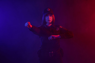 Redheaded female police officer is posing for the camera against a black background with red and blue backlighting.
