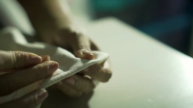 Close up of asian hand seamstress sewing a white clothes. Female seamer uses needle and thread by hand according to the ancient tradition. Slow motion shot in low light in vintage style.