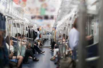 In the morning, many people, both men and women are standing and sitting on the subway who are travelling to work. In the city of Tokyo Japan
