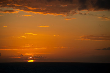 Carribean sun sets on the horizon taken at sea with backlit glowing orange cloud formations.copy space