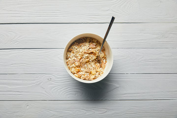 top view of breakfast cereal in bowl with spoon on wooden white background