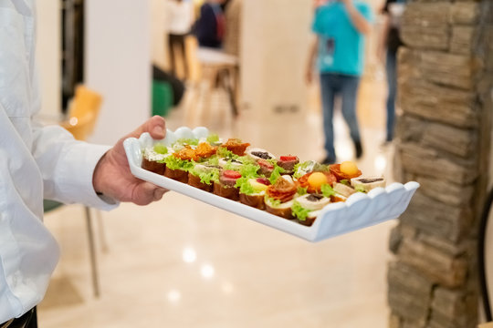 Waiter holding tray of mini sandwich appetizers.