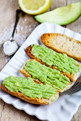 Croutons with avocado guacamole on white plate closeup on rustic wooden table.