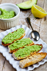 Toasts with avocado guacamole on white plate closeup on rustic wooden table. Diet breakfast.