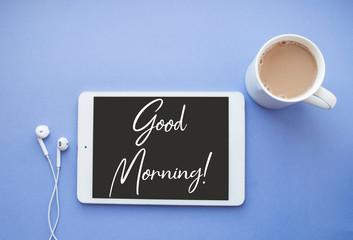 Flat lay of white tablet, earphones and a cup of coffee on purple background with copyspace.