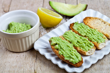 Crostini with avocado guacamole on white plate closeup on rustic wooden table. Diet breakfast. Delicious and healthy plant-based food.