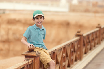 Boy in the cap is sitting at the wooden fence on the beach