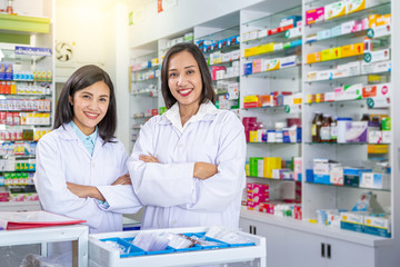 Fototapeta na wymiar Two smiling asian pharmacists crossing arms while staying in drugstore. Medicine, pharmaceutics, health care and people concept. 