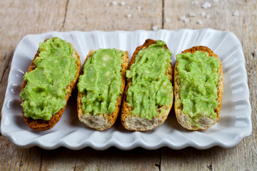 Fresh crostini with avocado guacamole on white plate closeup on rustic wooden table.