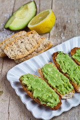 Fresh crostini with avocado guacamole on white plate closeup on rustic wooden table.