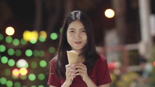 Asian young woman travel in Bangkok, Thailand, beautiful female feeling happy walking and eating ice cream at The Khao San Road. Women travel eat street food in Thailand concept. Slow motion shot.