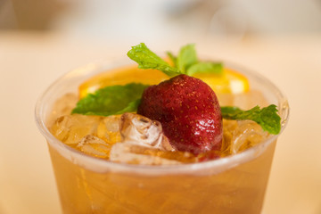 Beverage mocktail orange flavor, mixed with lime and strawberry with ice decorated with mint leaves in a plastic glass.