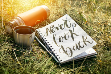 Never look back word written in white notebook with pen and red cup thermos on the green grass. Outdoor Concept hand writing showing Never Look Back, No regrets