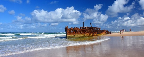 The rusty wreck of the vessel Maheno on the shores of Fraser Island (Queensland, Australia). The antique rusty and damaged boat and corrosion in the ocean sea. - obrazy, fototapety, plakaty