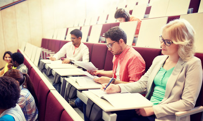 education, high school, university, learning and people concept - group of international students writing test at lecture hall