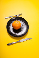 One orange on black plate on retro yellow background. Abstract concept of healthy food