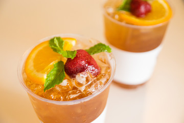 Beverage mocktail orange flavor, mixed with lime and strawberry with ice decorated with mint leaves in a plastic glass.