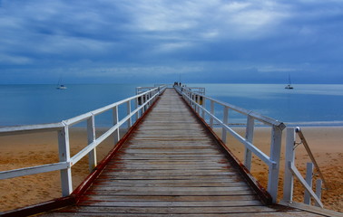 Fototapeta na wymiar Great views of Hervey Bay from the wooden Torquay jetty. The pier is also a popular fishing spot at all tides. Gushing sea on a cloudy day. Horizontal view of dramatic overcast sky and sea.