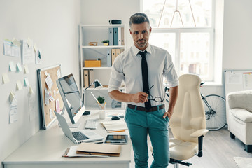 Ready to work. Good looking young man looking at camera and smiling while standing in the office