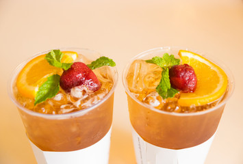 Beverage mocktail orange flavor, mixed with lime and strawberry with ice decorated with mint leaves in a plastic glass.