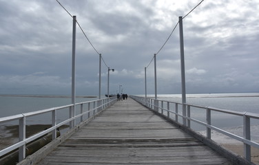 Great views of Hervey Bay from the wooden Urangan pier. The pier is also a popular fishing spot at all tides. Gushing sea on a cloudy day. Horizontal view of dramatic overcast sky and sea.