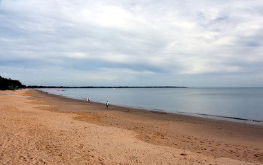 Panoramic landscape of Torquay beach in Hervey Bay (Queensland, Australia) on a cloudy day. People walking on the beach at low tide.