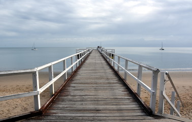 Fototapeta premium Great views of Hervey Bay from the wooden Torquay jetty. The pier is also a popular fishing spot at all tides. Gushing sea on a cloudy day. Horizontal view of dramatic overcast sky and sea.