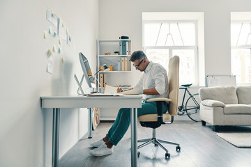 Very busy. Good looking young man writing something while sitting in the office