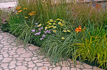 A flower border with Grasses Daylillies Anthemis tinctoria and Achillea bordering a decorative terrace