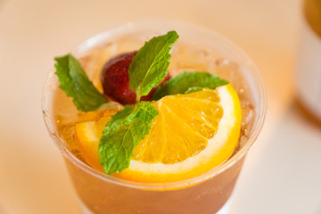 Beverage mocktail orange flavor, mixed with lime and strawberry with ice decorated with mint leaves in a plastic glass.