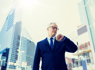 business, punctuality and people concept - senior businessman checking time on wristwatch or smart watch on his hand in city