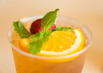 Beverage mocktail orange flavor, mixed with lime and strawberry with ice decorated with mint leaves in a plastic glass.