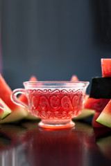 Vertical shot of fruit ice tea of watermelon seeds in a transparent glass cup on wooden surface along with triangular pieces of watermelon.