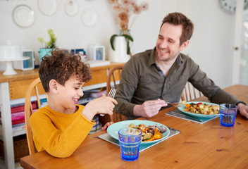 Single Father Sitting At Table Eating Meal With Son In Kitchen At Home