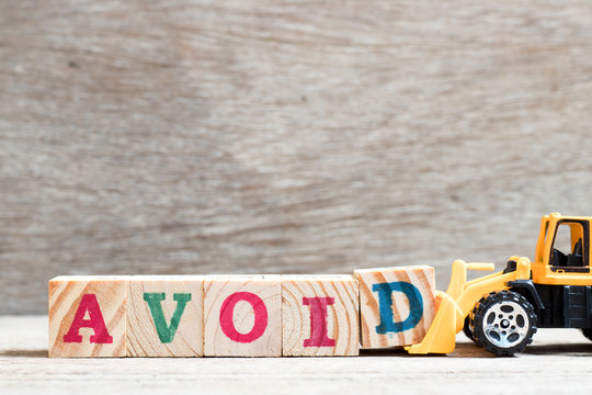 Toy bulldozer hold letter block d to complete word avoid on wood background