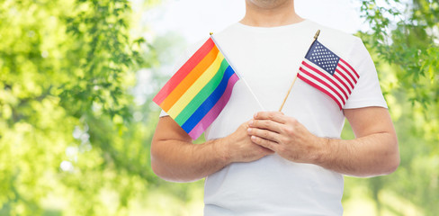 lgbt, same-sex relationships and homosexual concept - close up of man wearing gay pride rainbow awareness wristband and holding american flag over green natural background