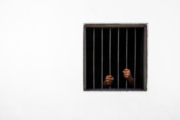 Hands of the prisoner on rusty bar of the window and prison cell white cement wall