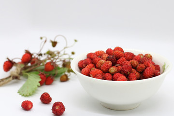 bouquet of wild strawberries close-up on a white background near a plate of berries