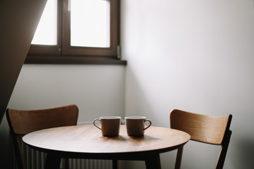 Fototapeta na wymiar Two cups on wooden table. Dining room with table and two chairs. Modern minimal Scandinavian nordic interior. Morning coffee